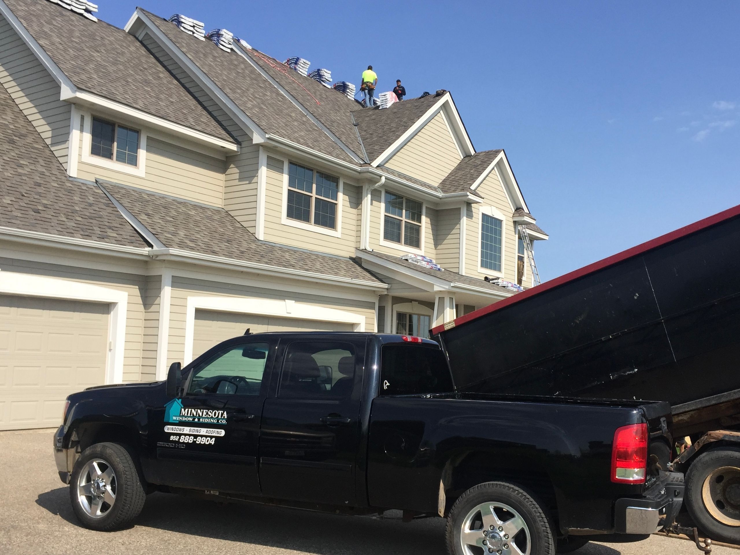 Company pickup and dump trailer parked for a tear-off with the crew working on the roof behind