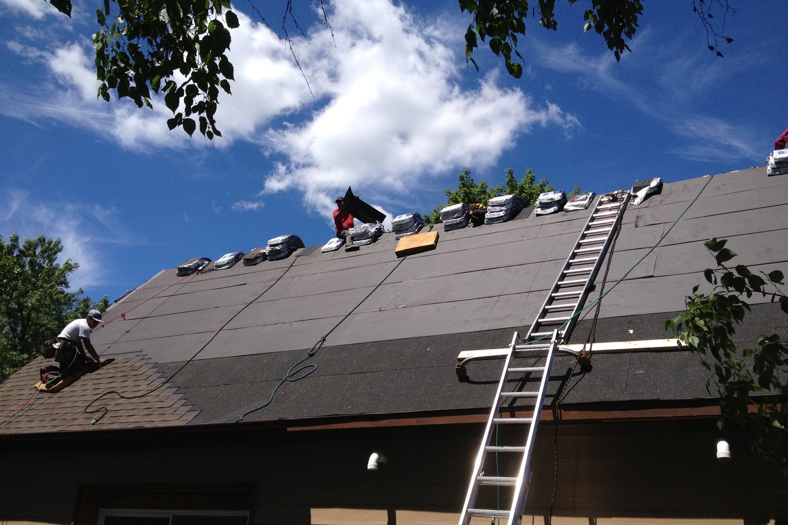Roofers laying new shingles over fresh underlayment on a steep roof